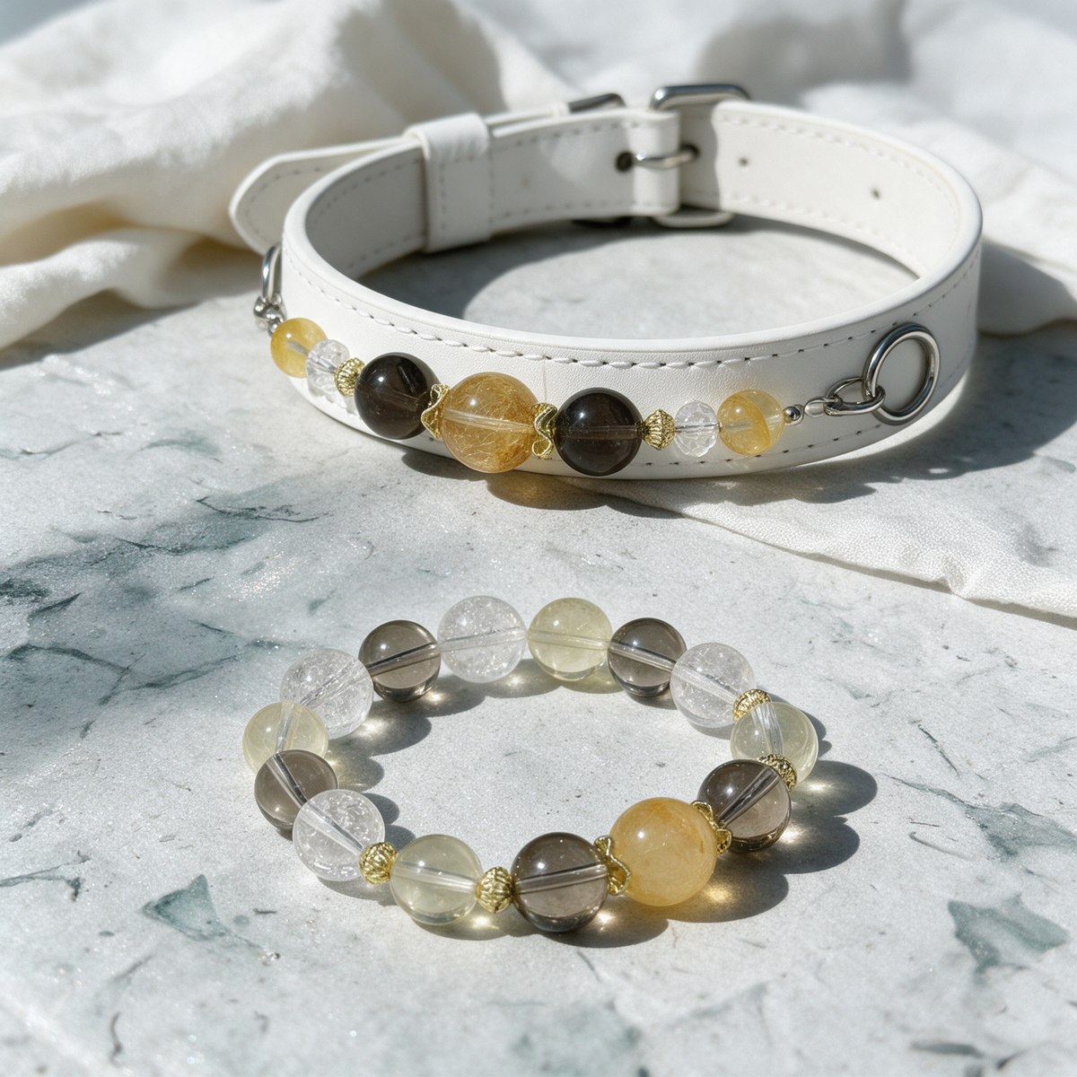 Close-up of the Champagne Light white collar and matching bracelet on pale stone, showing golden, smoky-brown and clear bead details.